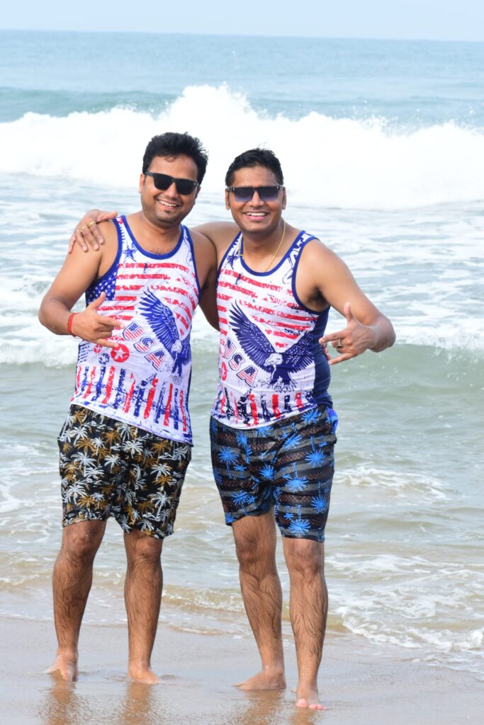 Harsh and Neeranjan Kumar enjoying a serene moment at Rishikonda Beach, Visakhapatnam, with waves crashing and the sun setting in the background.