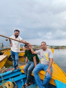 Abhilash Yadav and Harsh Nema at Vizag Fishing Harbour posing with colorful fishing boats in the background

